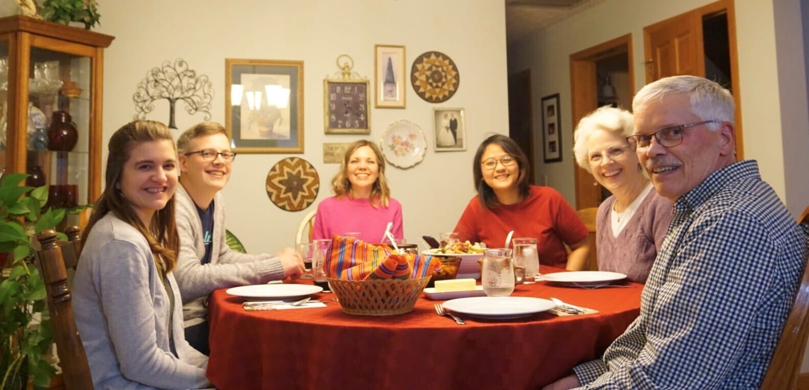 A group of six people sit around a dining room table. They are all smiling at the camera.
