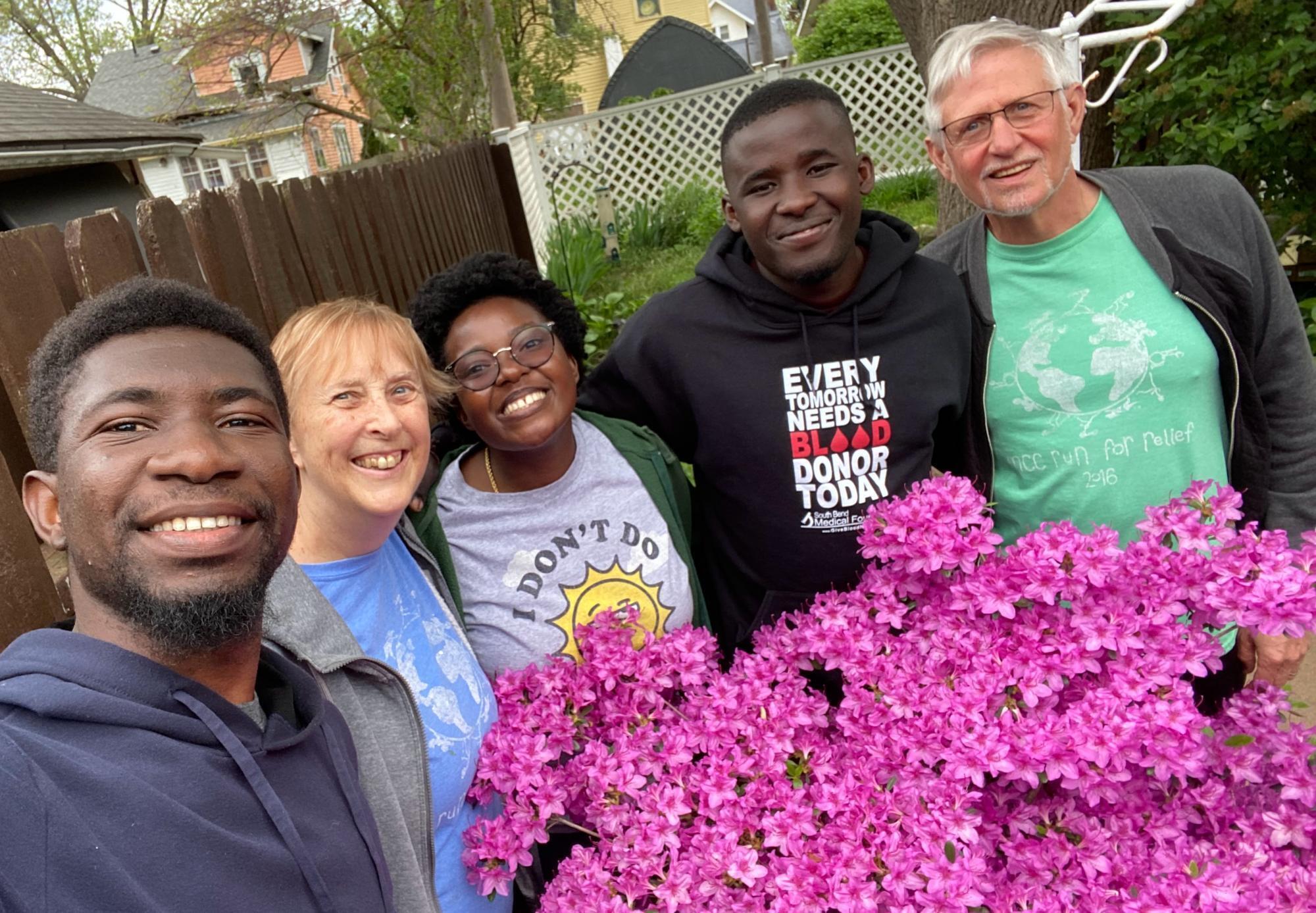 Three young adults from Africa take a photo with their host parents from the United Stated. They are standing behind a pink flowering bush.