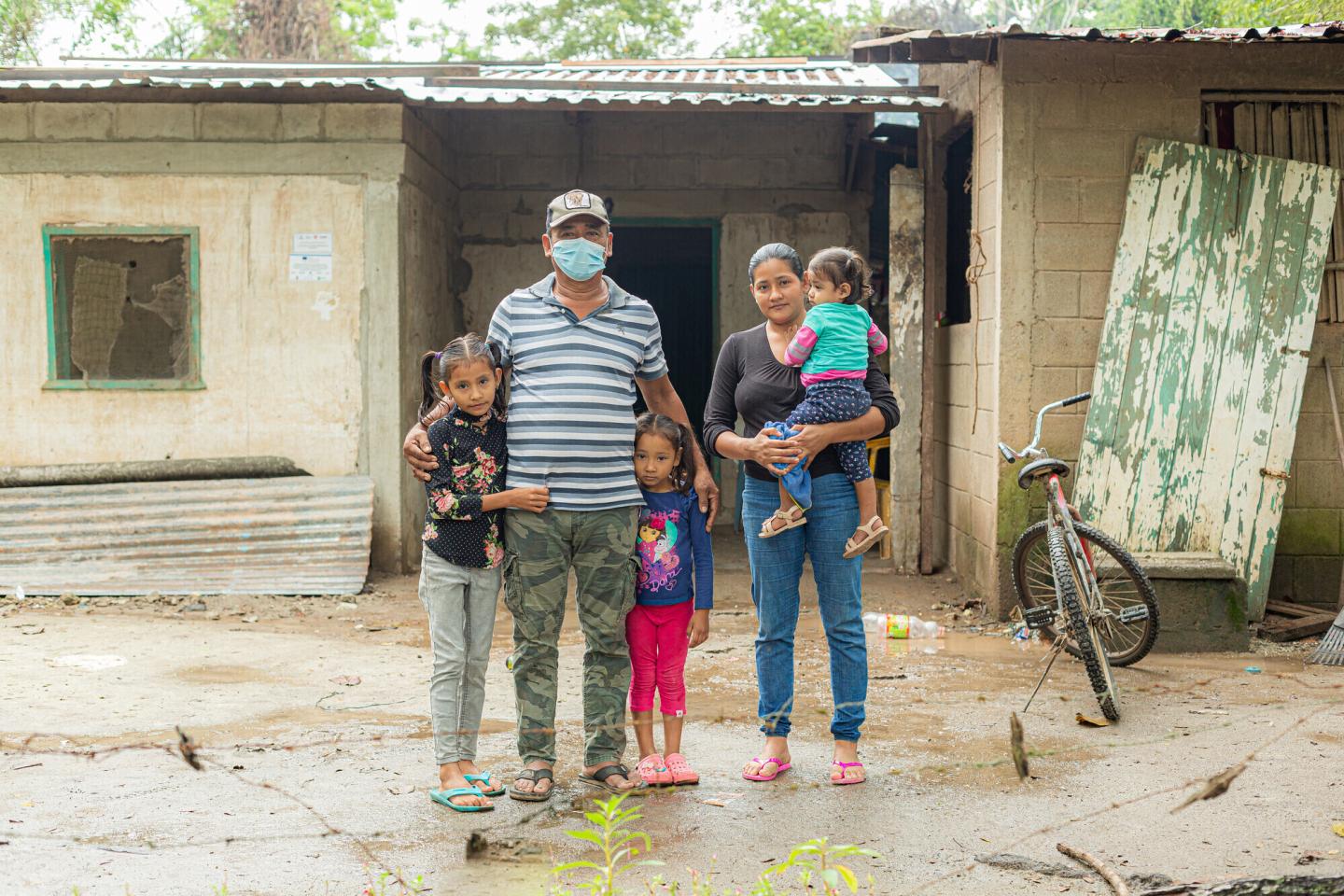 A Honduran family of five stands in front of their home.