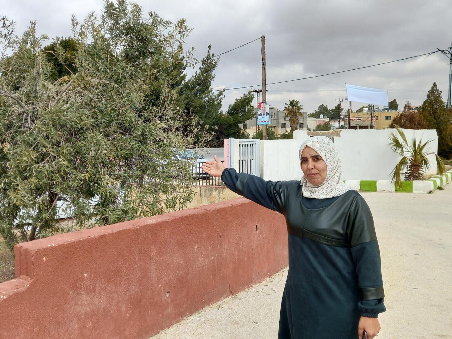 A Jordanian woman in a hijab gestures towards a tree on the left.