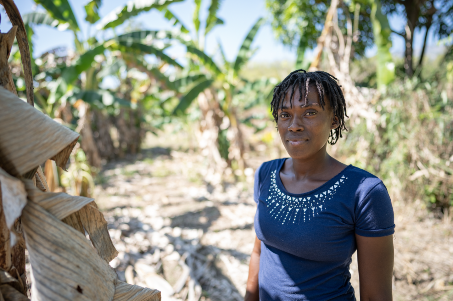 A Haitian woman in a blue shirt stands in a field