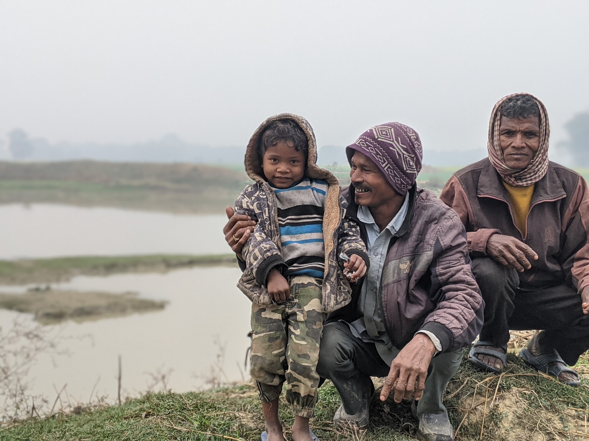 Two Nepali men squat next to a child near fish ponds.