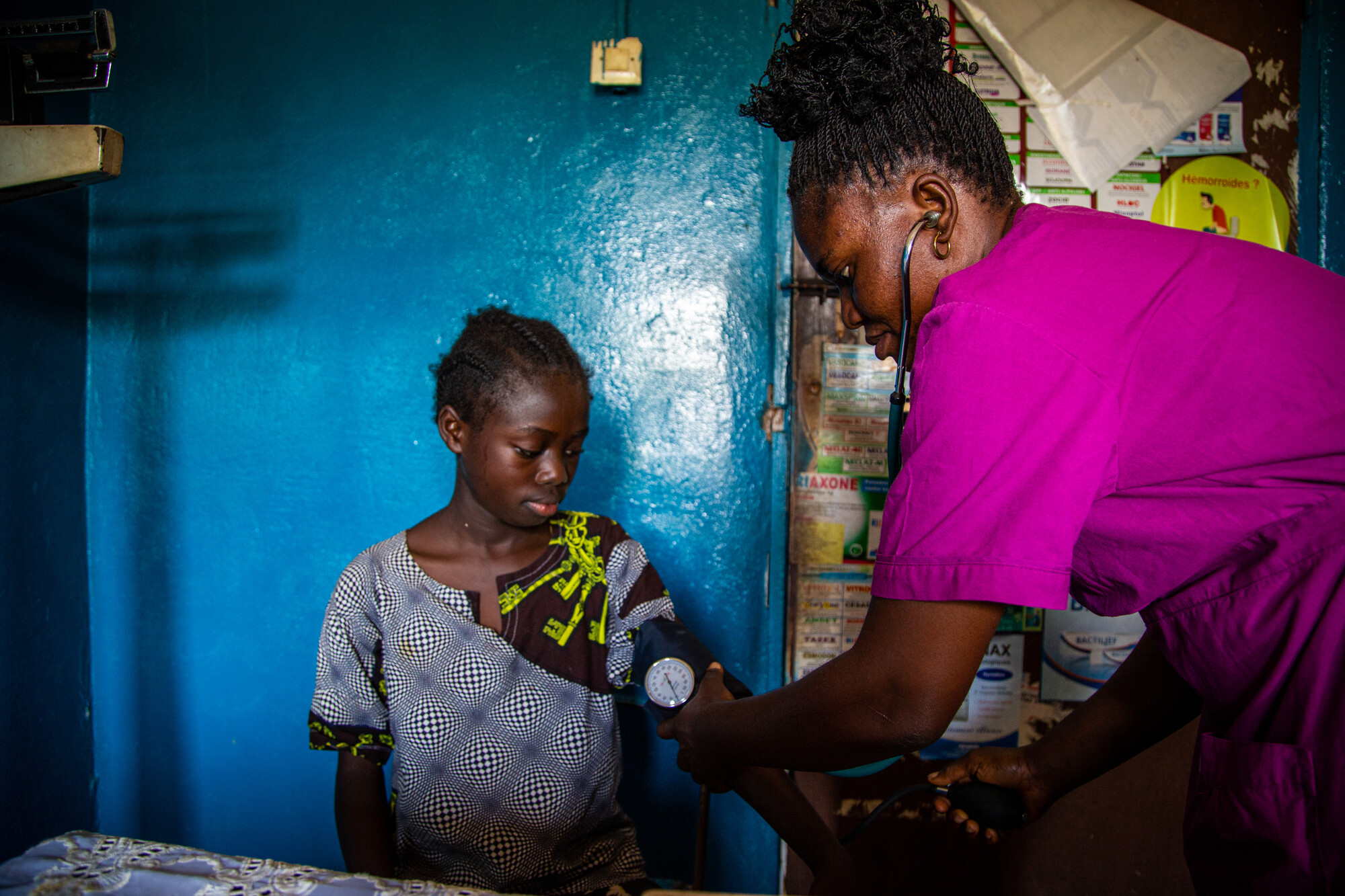 A nurse in pink scrubs takes the blood pressure of a young patient