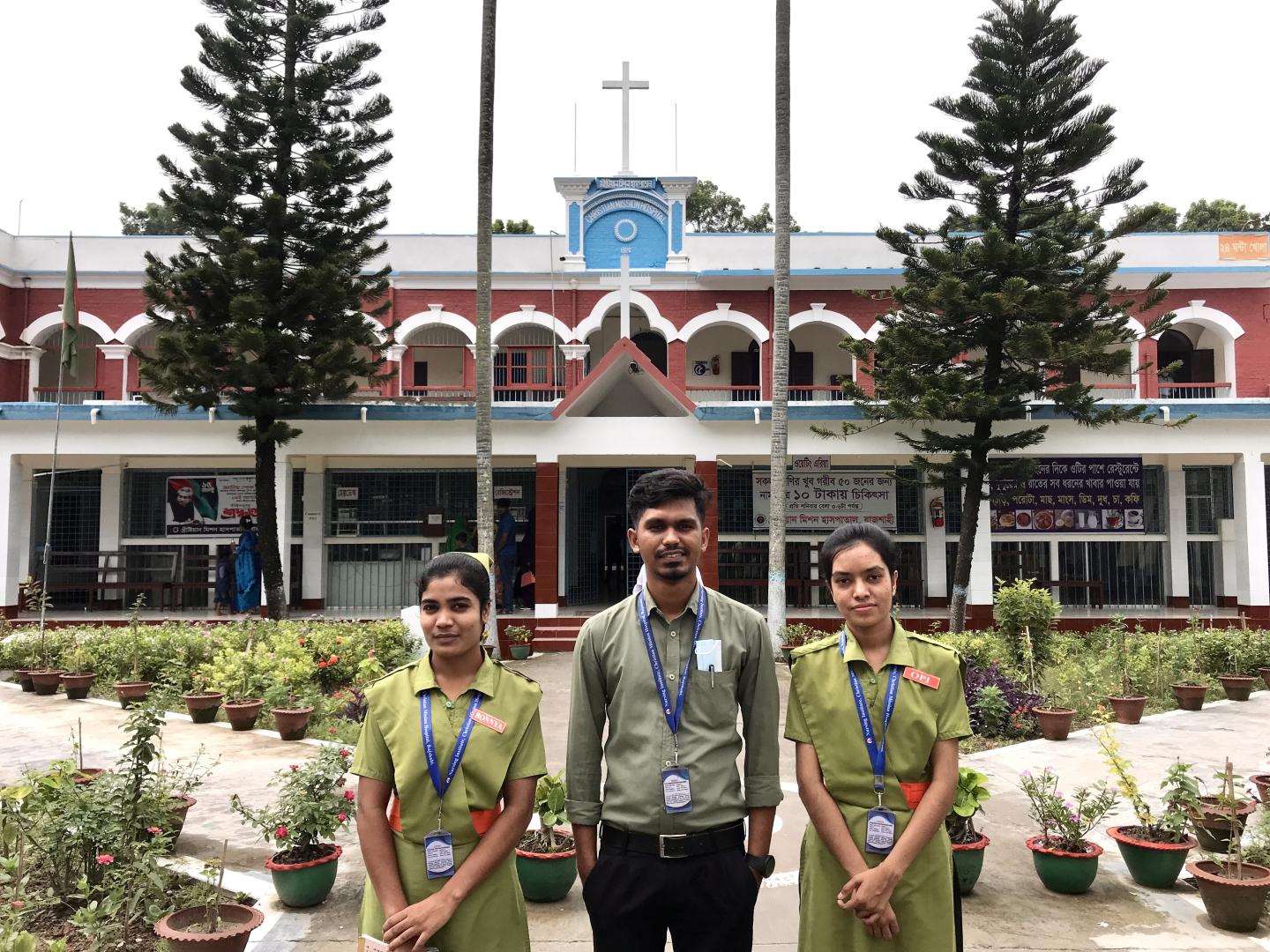Three nursing students stand in front of a red building
