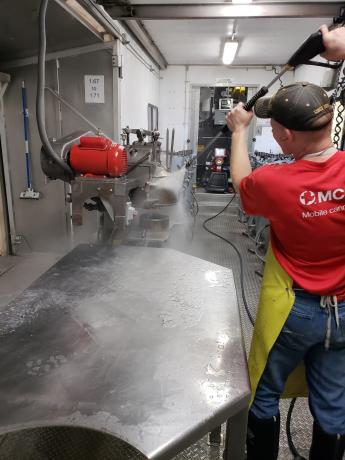 A man in a red shirt cleans a food processing area