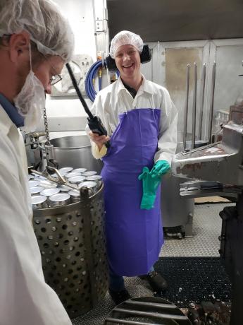 A man in a purple apron and hair net smiles for the camera