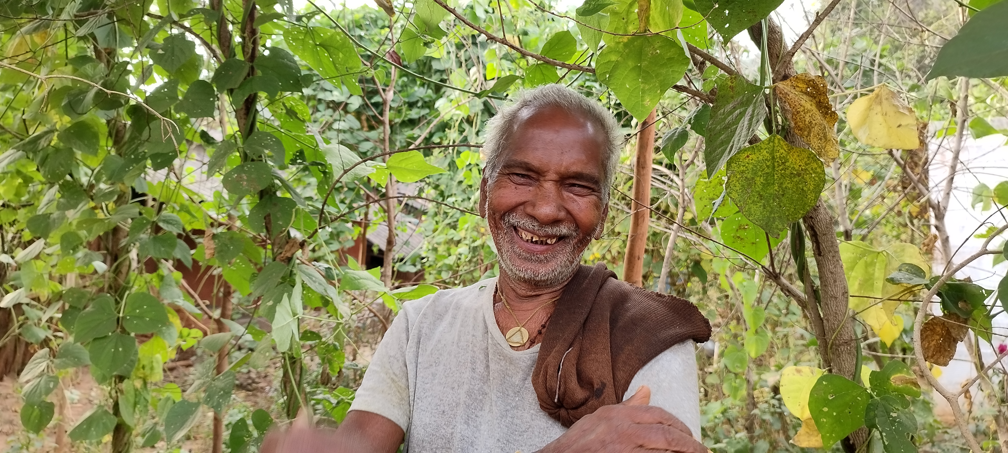 Parma Bardaset, a farmer from Bhutadi, India smiles as he stands in front of bean plants he grew in his kitchen garden.