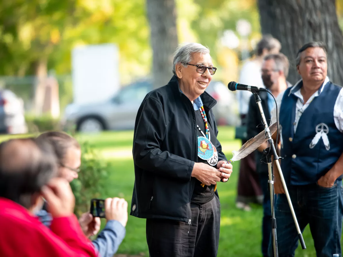 An Indigenous elder speaks into a microphone during an outside event.