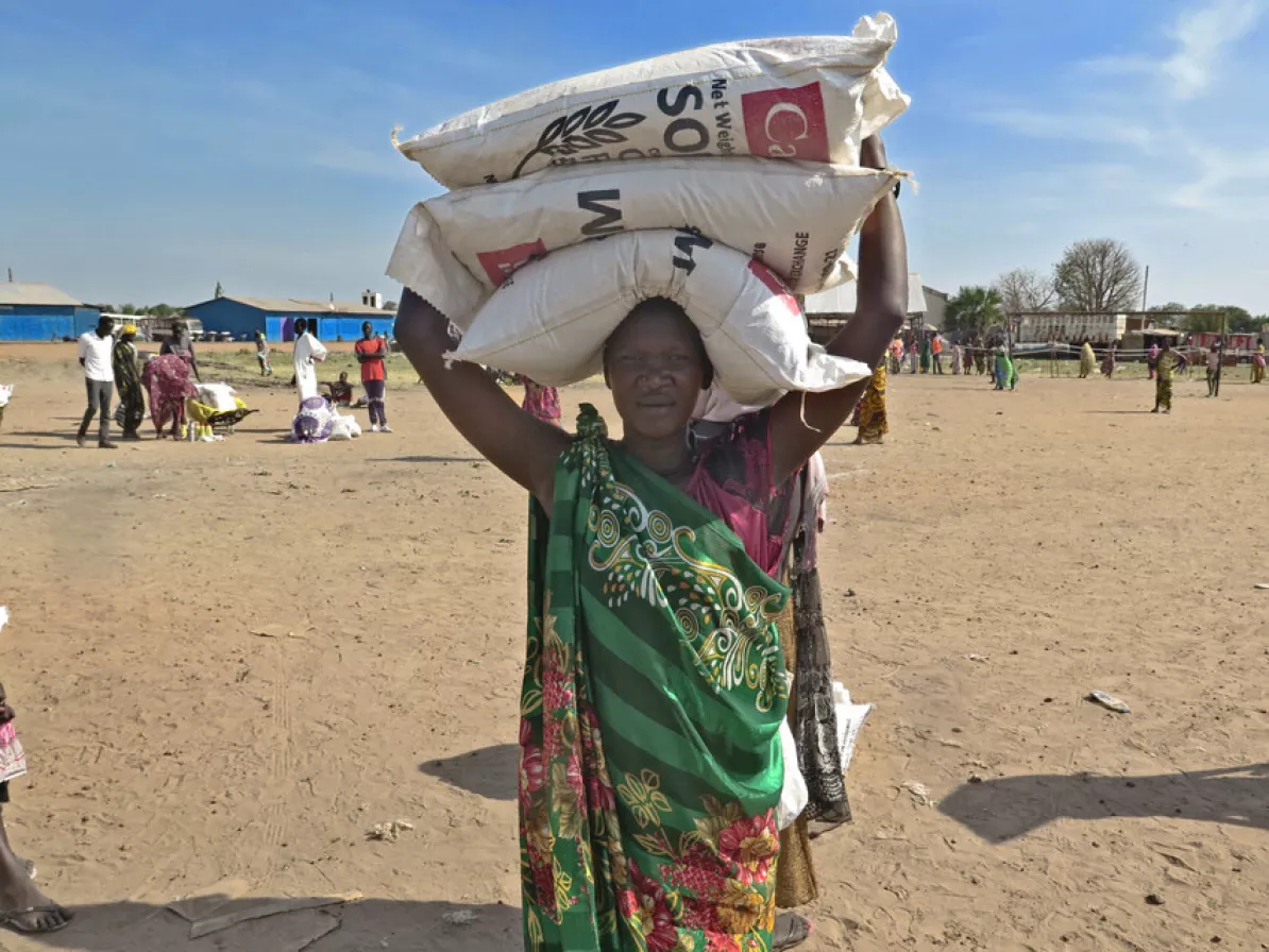 Nyachar Kueth Kang carries bags of sorghum she received during a May 2021 distribution of food assistance in Rubkona county, South Sudan, by the relief and development agency of the Episcopal Church o