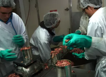 A group of people filling cans with meat