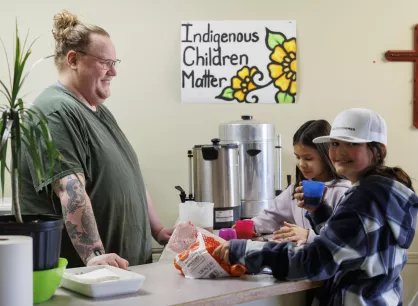 A person behind a counter serves drinks to two young girls who are helping themselves to oranges