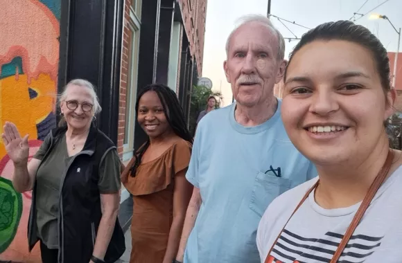 Two older people and two young adults stand together in front of a colorful building.