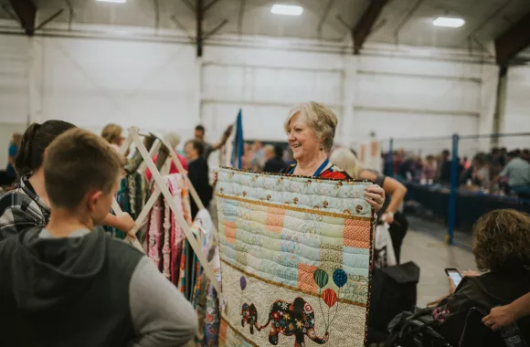 Volunteer holding up a quilt for customers.