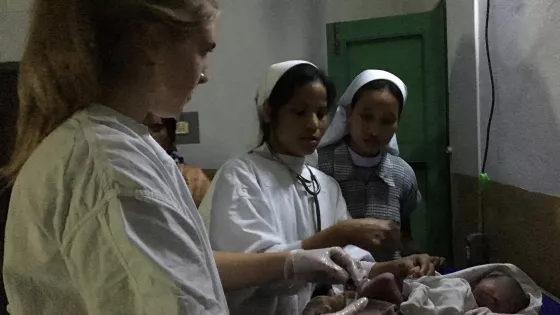 Three nurses in white work with a newborn baby