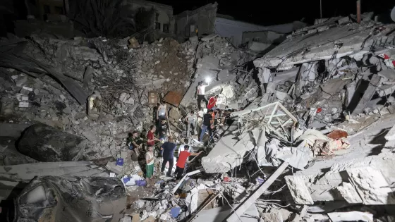 A crowd searches the crater of a destroyed building at night