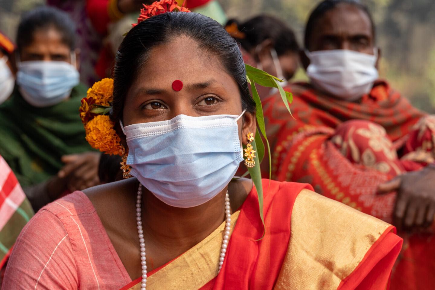 A Bangladeshi woman with flowers in her, wearing a face mask and a red bindi 