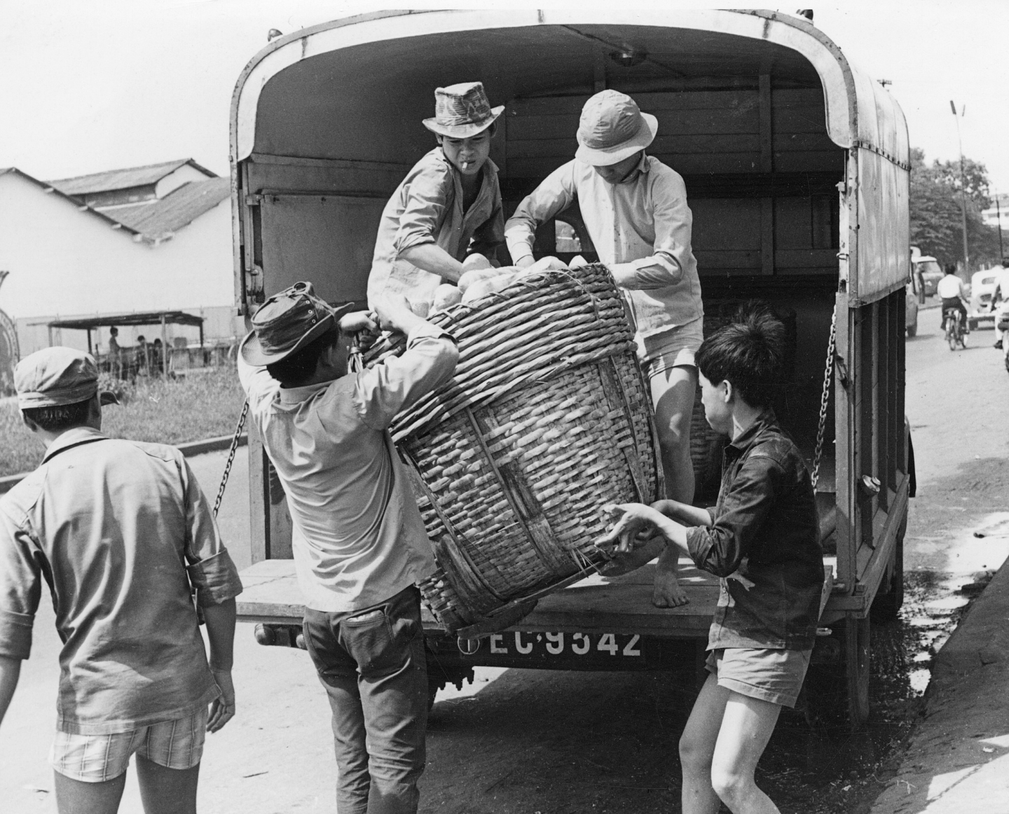 A black and white photo from the 1960s of men loading a large basket into a back of a truck in Vietnam