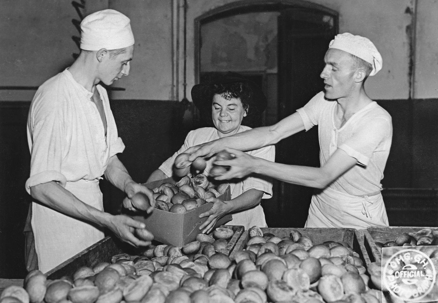 A black and white photo from teh 1940s of three people putting bread rolls into a box