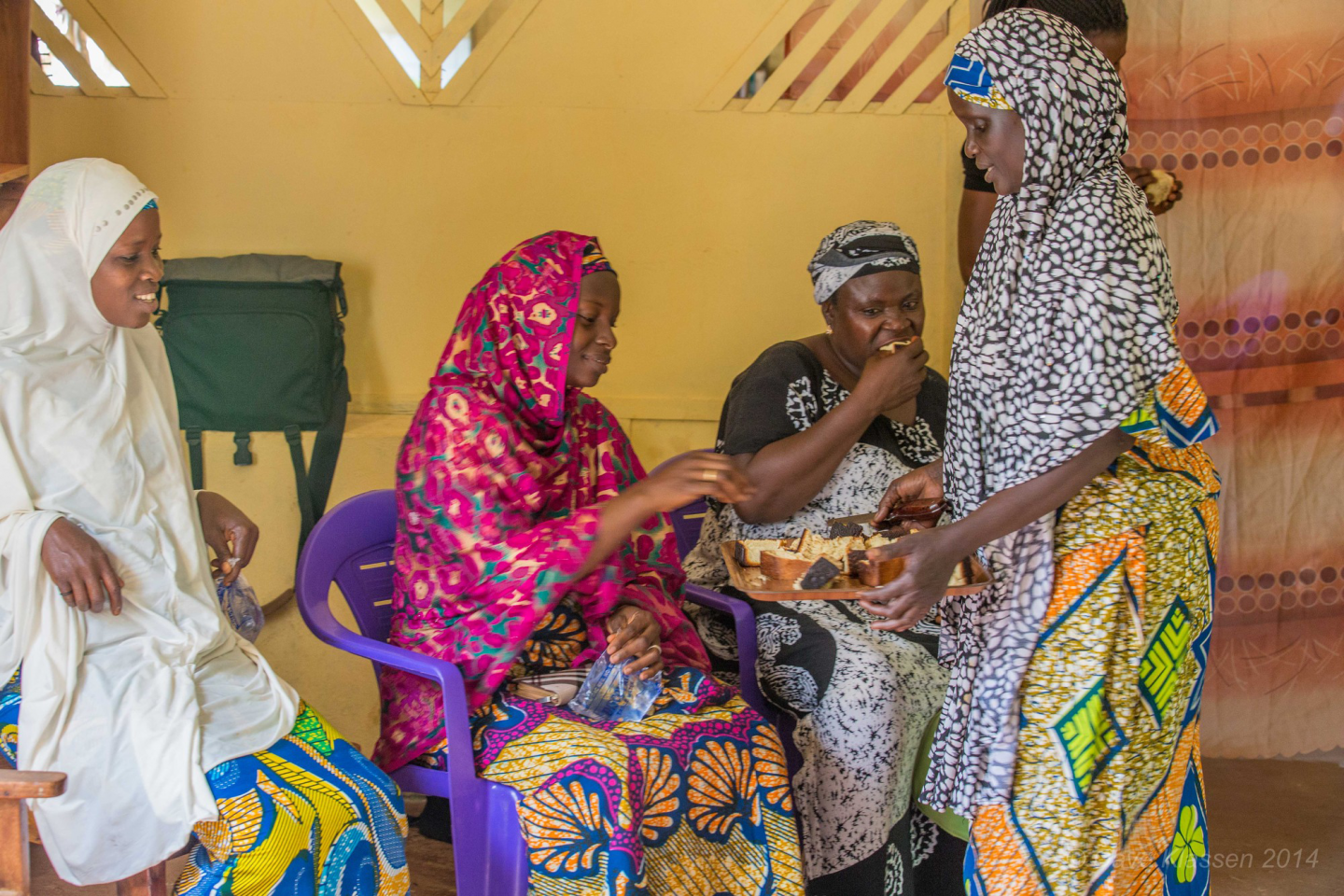 A Nigerian woman serves three other women (who are sitting down) pieces of bread