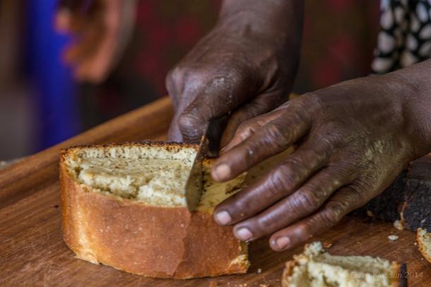 A close up of hands cutting a piece of bread with a knife