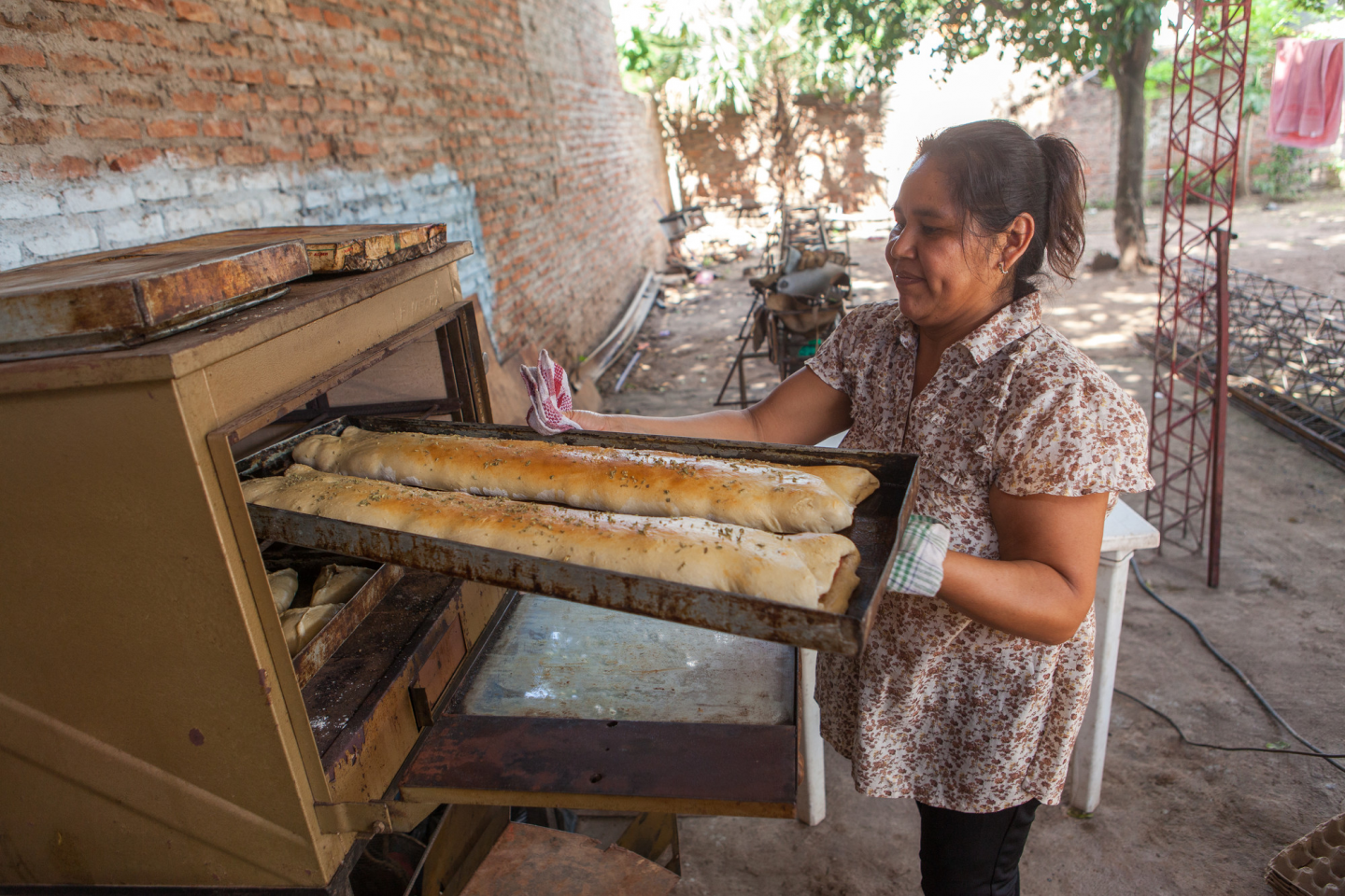 A Bolivian woman pulls out a tray of baked bread from an outdoor oven