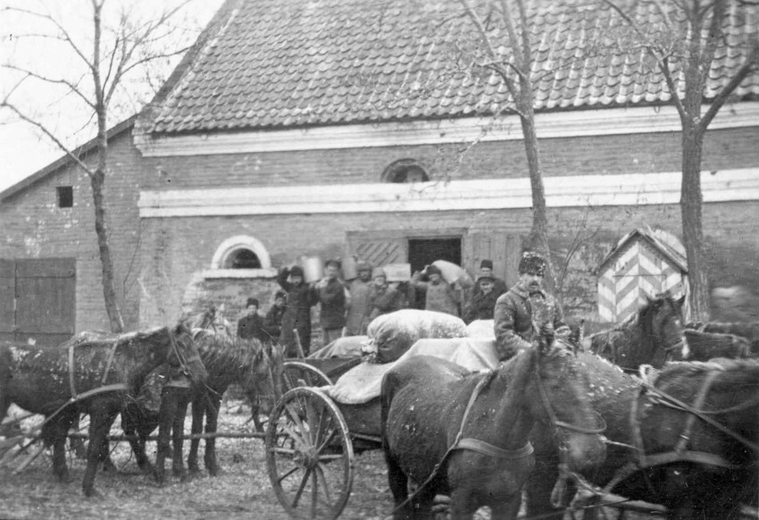 A black and white photo from the 1920s of a man in a wagon full of supplies. There are more men in the background holding supplies