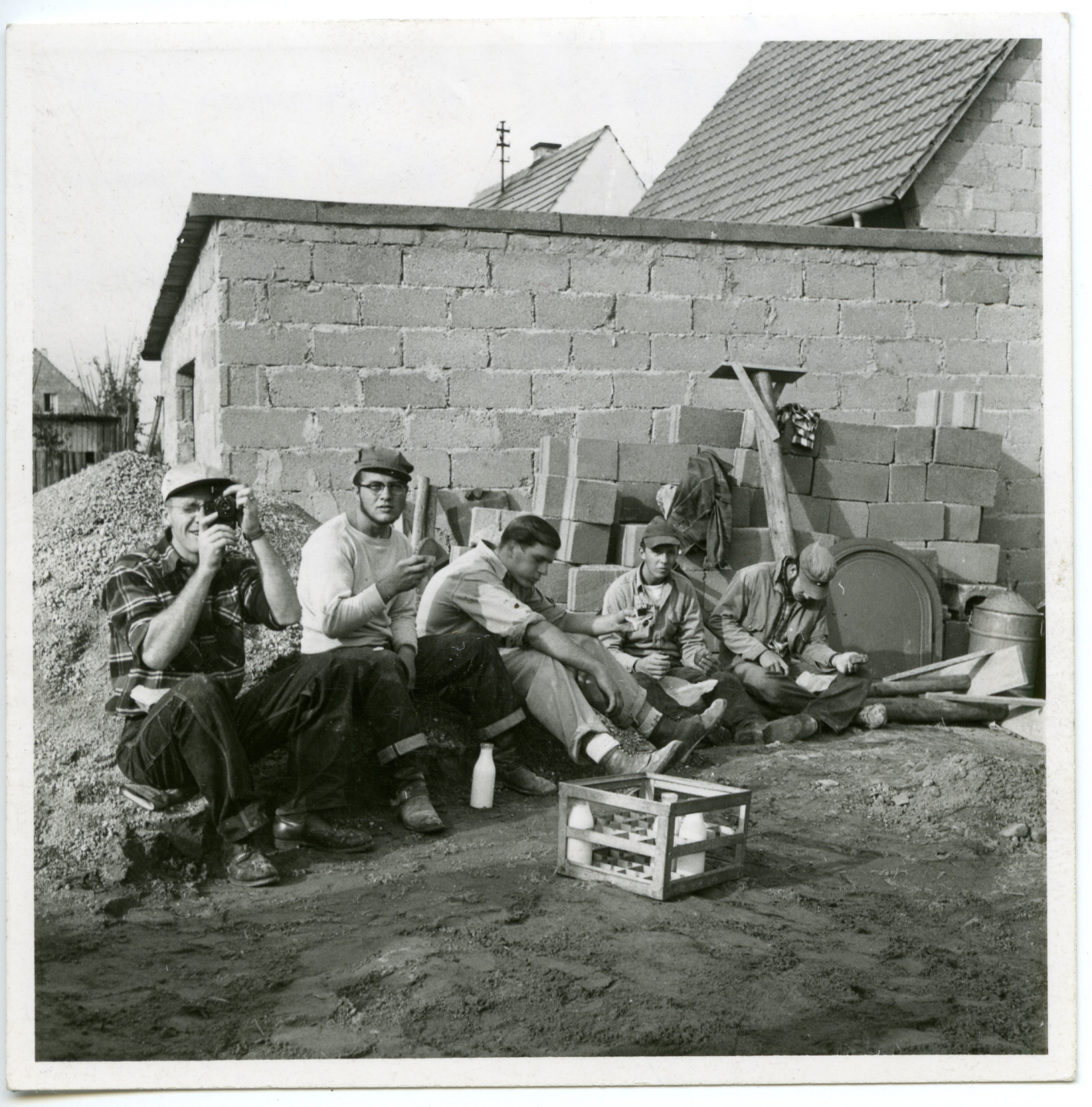 A black and white photo from the 1950s of men taking a break from their work to have a snack