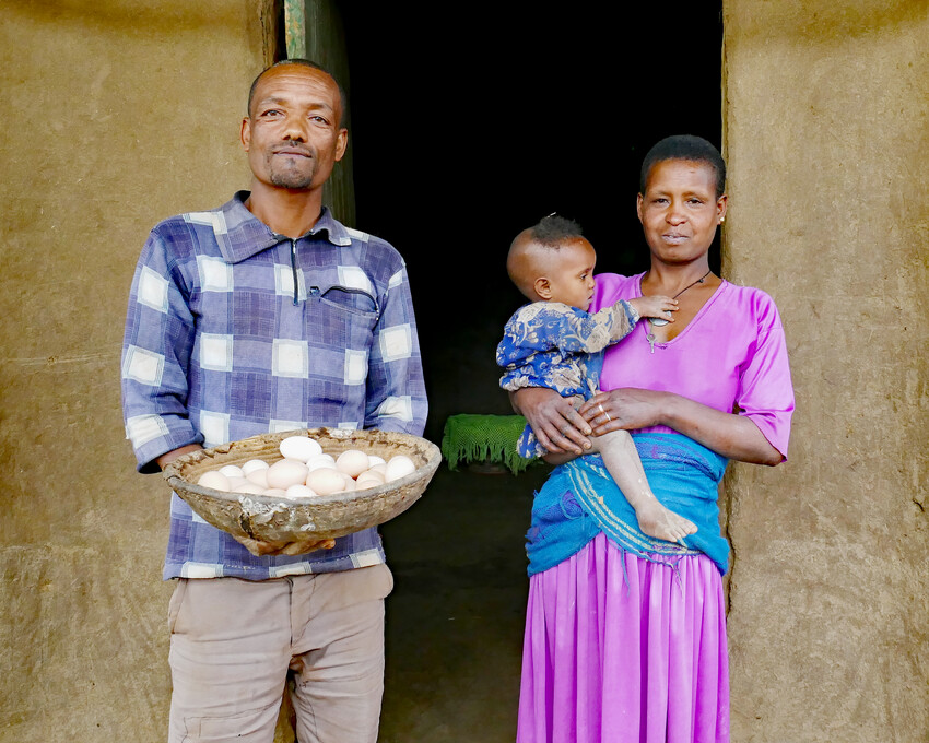 Atalay Ebestu stands in front of his house with his wife Bachu Tilahun, and their youngest child Zenebu Atalay. Atalay is holding a basket of eggs produced by their small flock of chickens, to be used