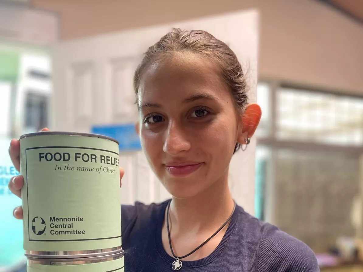 A young adult holds two cans with green labels that are stacked on top of each other