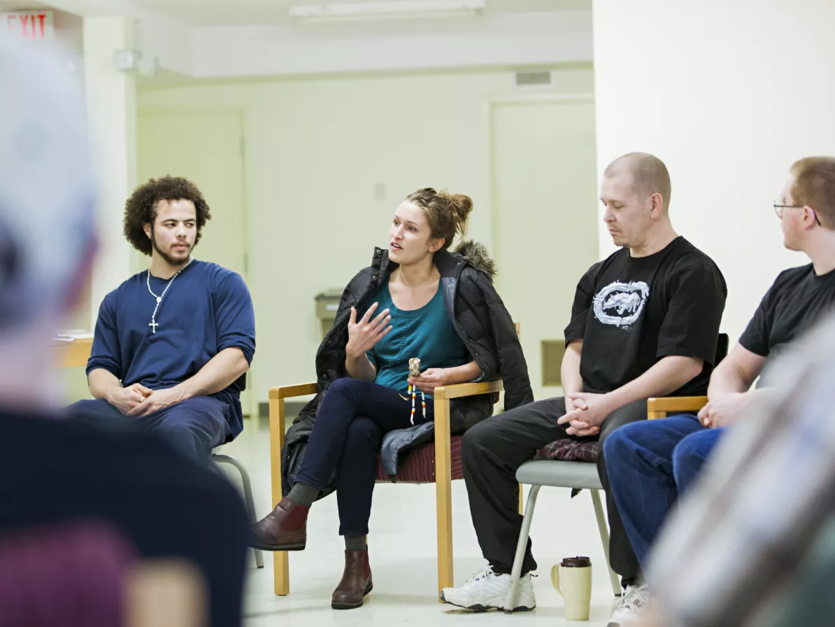 A woman speaks to a group who are all sitting in chairs in a circle