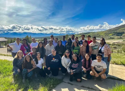 A large group of young adults pose for a photo. In the background is a mountain range.