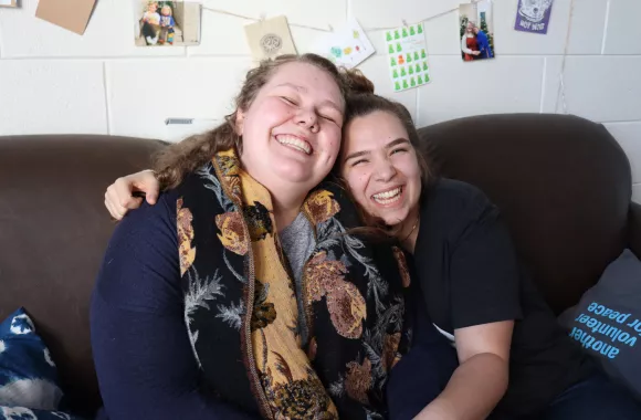 Two young women sit on a couch in a dorm room 