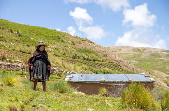 Woman standing on a green hill with blue sky and terraced fields in the background.