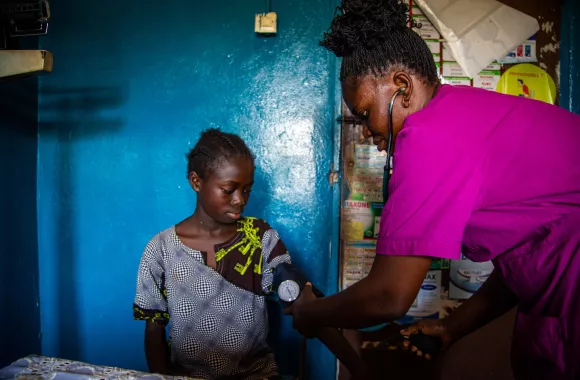 A nurse in pink scrubs takes the blood pressure of a young patient