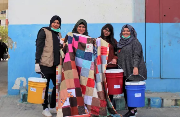 Four women stand together and pose with a comforter and three five-gallon buckets.